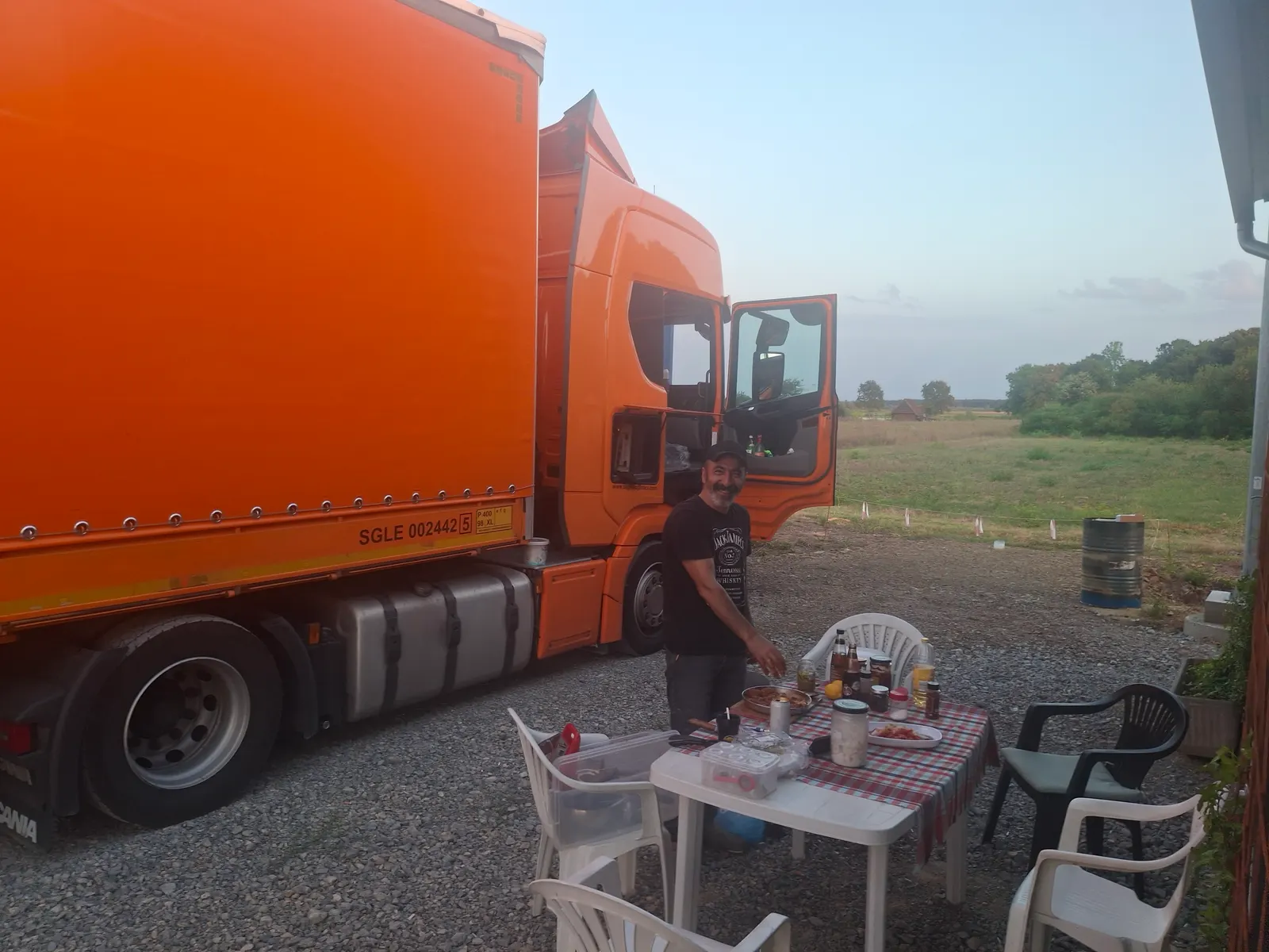 Vozač postavlja stol za večeru pokraj svog narančastog kamiona na parkingu, u sumrak